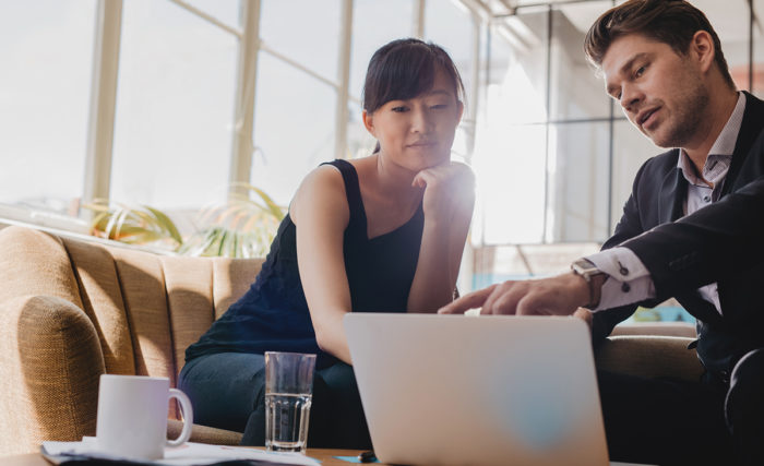 Shot of young woman sitting with businessman pointing at laptop screen. Business partners working together on laptop in office.